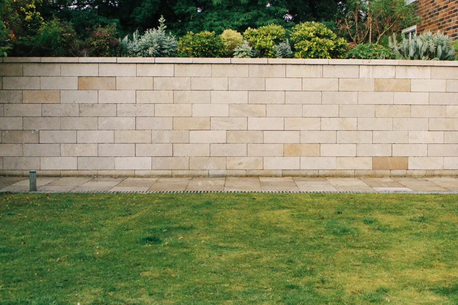 A stone retaining wall with planting above, paving and lawn.