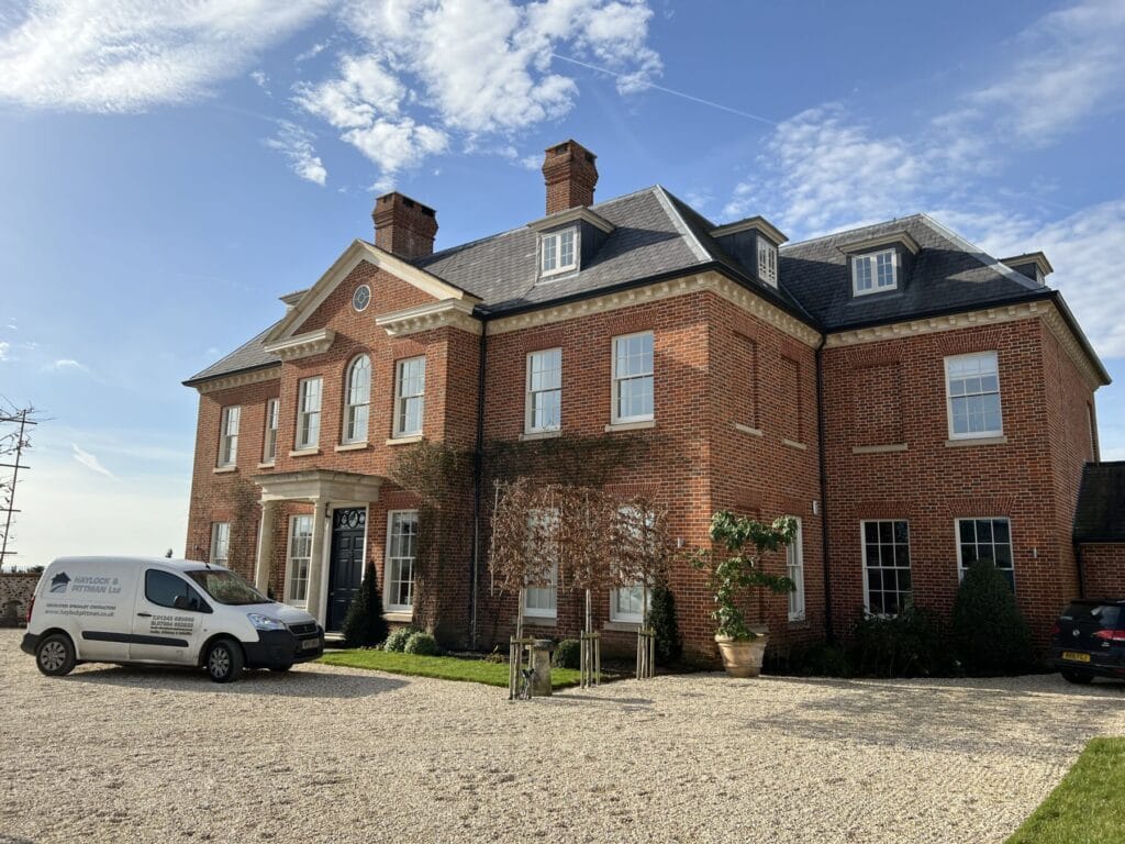 A substantial red-brick country house with a Haylock and Pittman van outside.