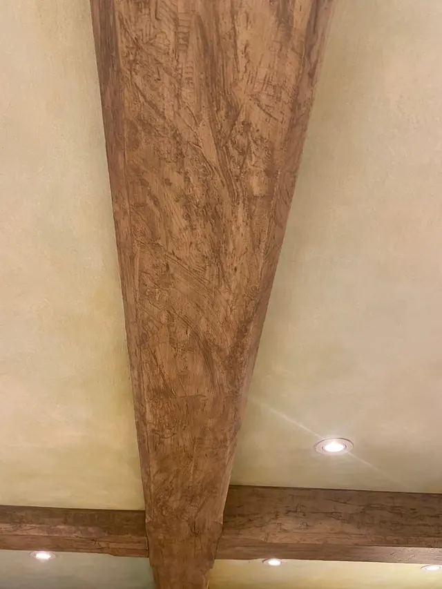 A ceiling beam painted to imitate burr walnut, meeting a limewashed vault.