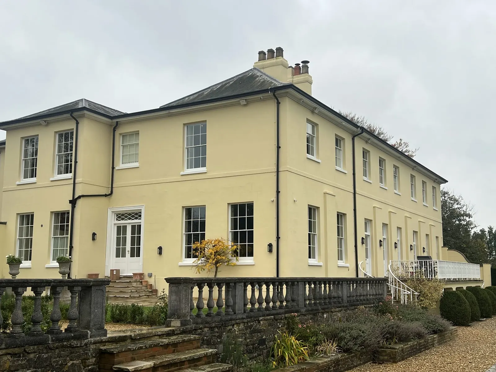 The garden front of the cream stucco house, with a stone balustraded terrace and steps down to the lawn.