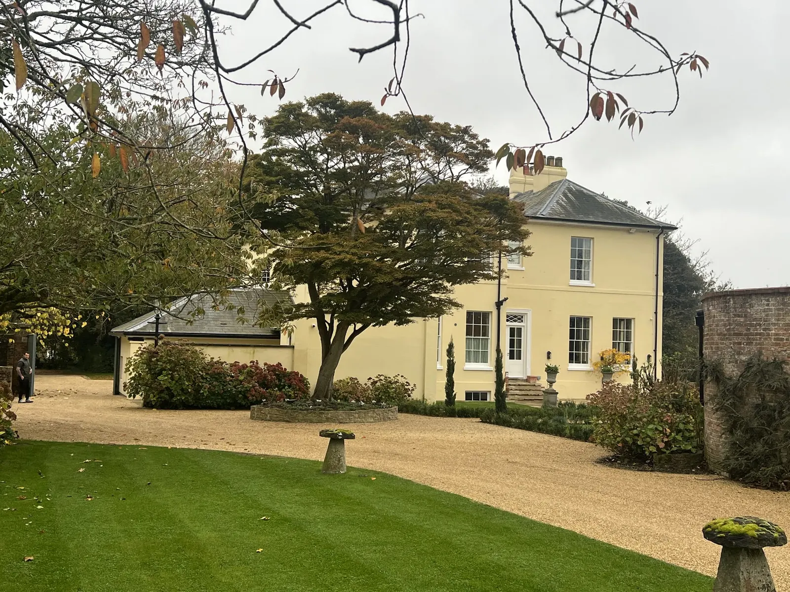 The approach across a striped lawn, with a staddle stone in the foreground and the cedar overhanging the drive.