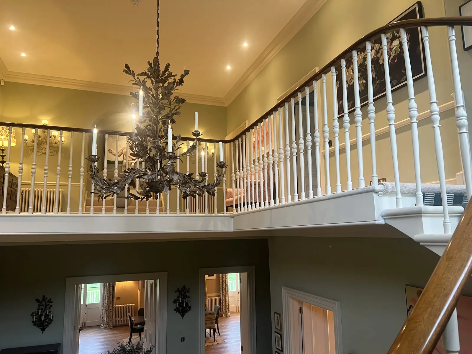 The double-height stair hall, with a galleried landing, white balustrade and a candle chandelier.