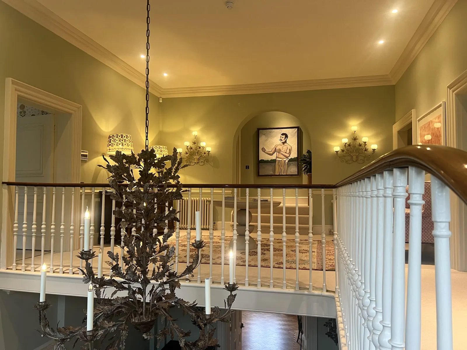 The landing lit at night, the wrought-iron chandelier hanging against warm yellow walls.