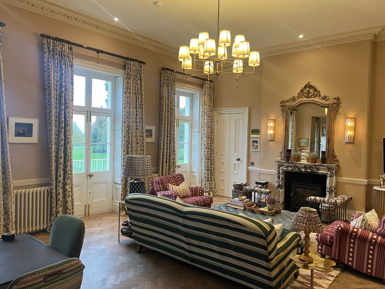A drawing room with a striped sofa, a gilt overmantel mirror and full-length curtains.