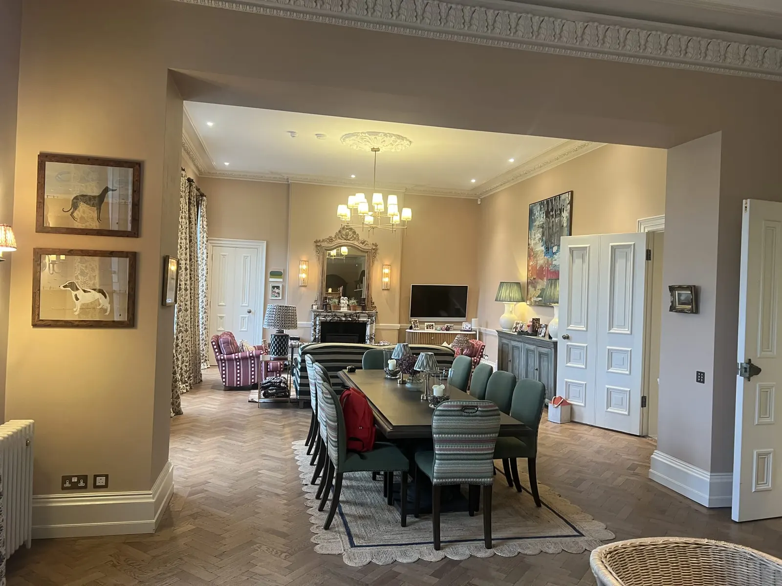 Through an opening into the dining room, long table laid, dog portraits on the wall.