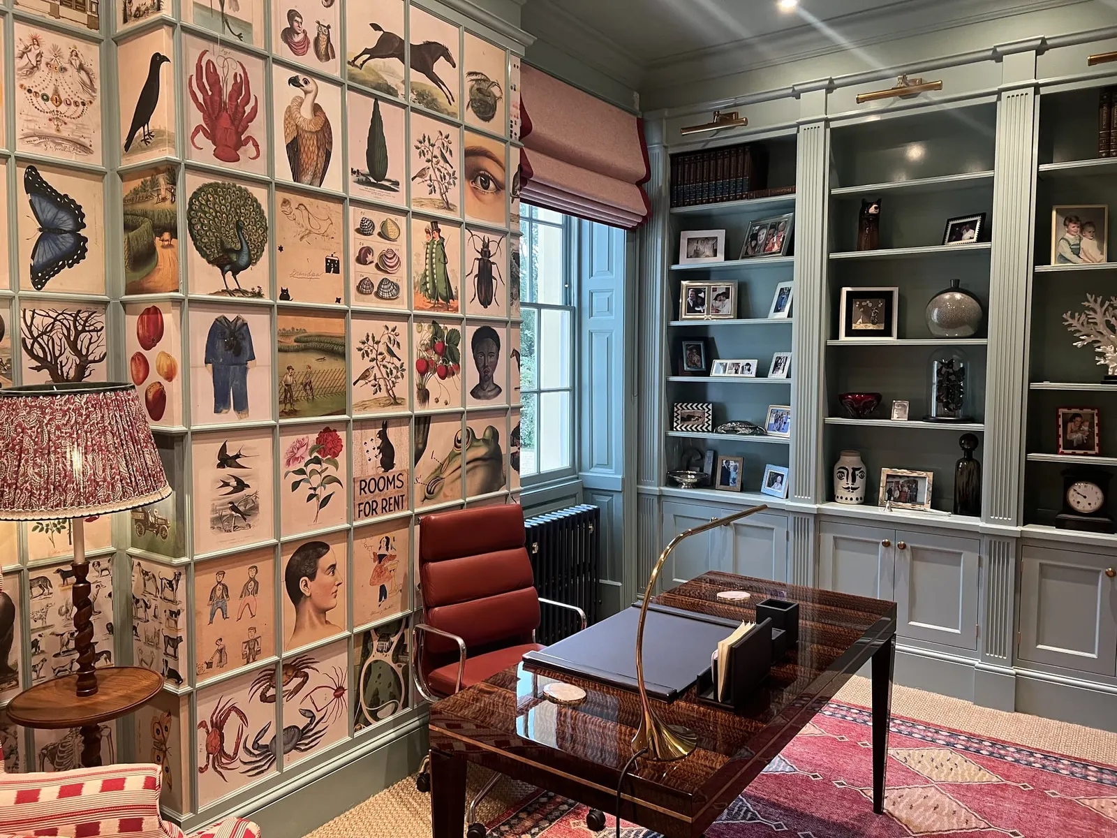 The study, its bookcase fronts covered in hand-applied natural history prints, with a red desk chair.