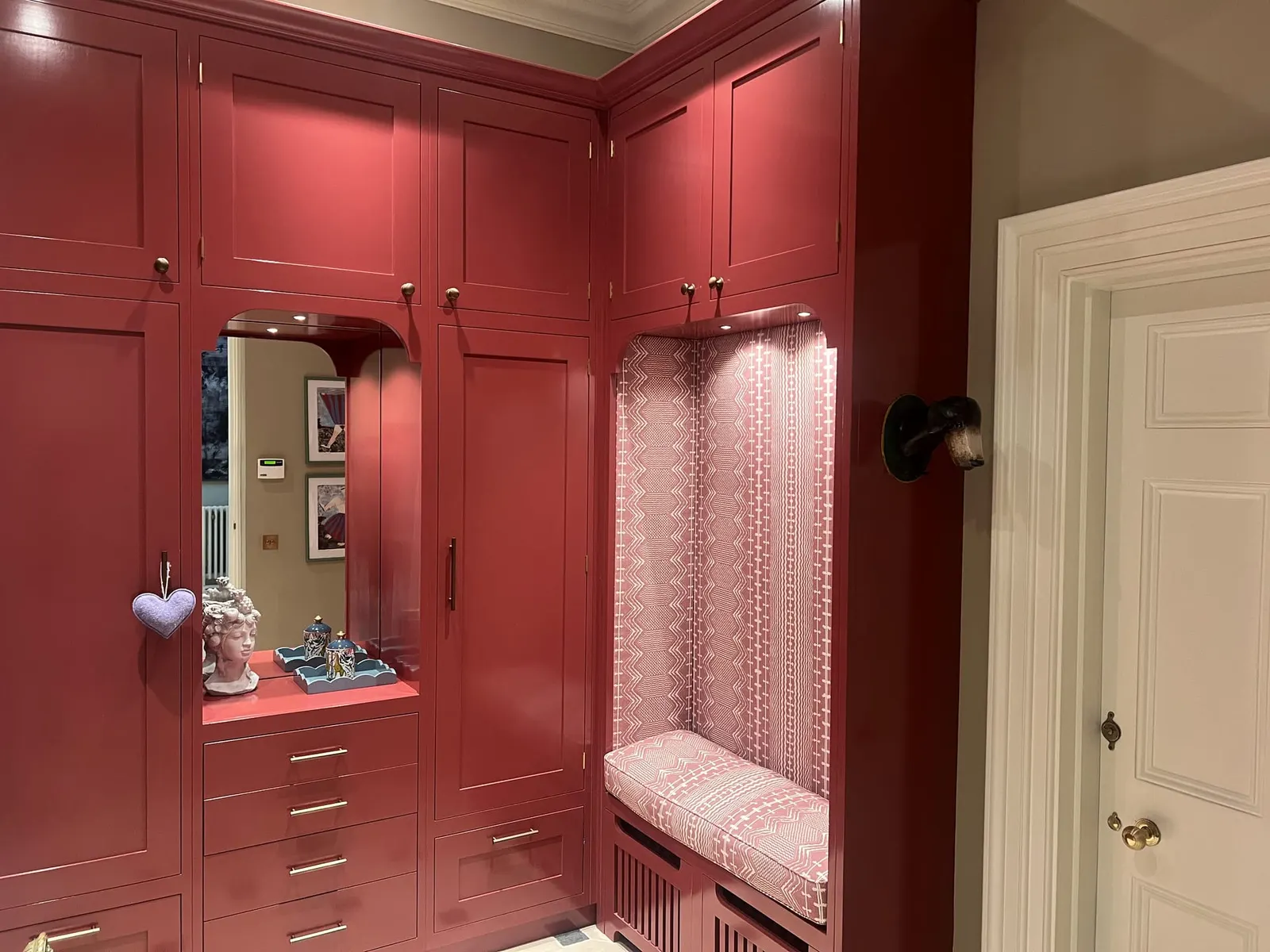 A dressing room panelled and painted deep red, with a lit alcove and an upholstered window seat.