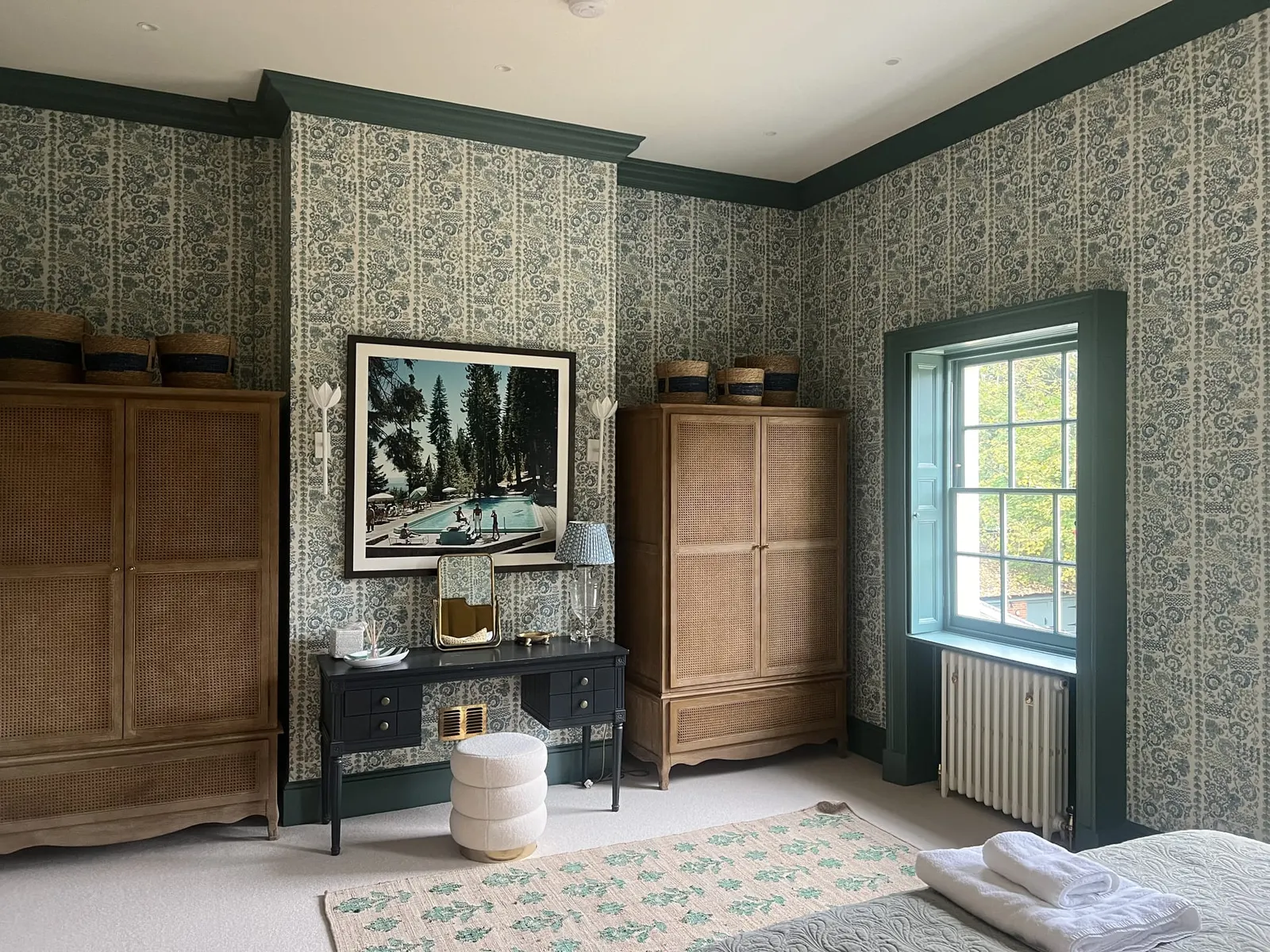 A guest room papered in a green leaf print, with limed oak wardrobes and teal painted window reveals.