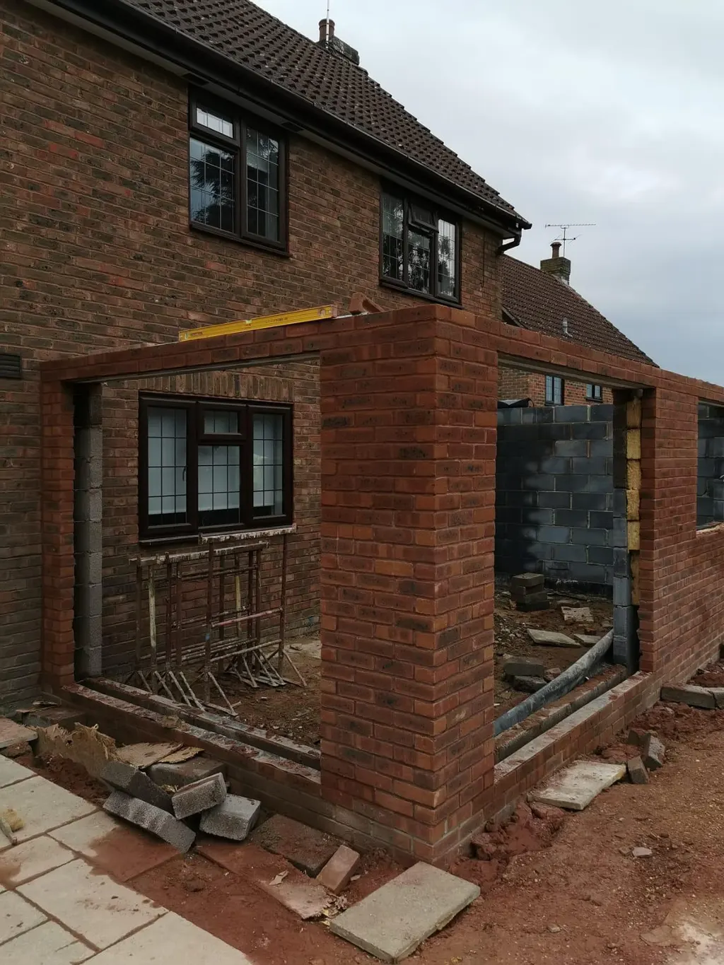 A brick extension shell against a detached house, openings formed and the inner leaf built in blockwork.