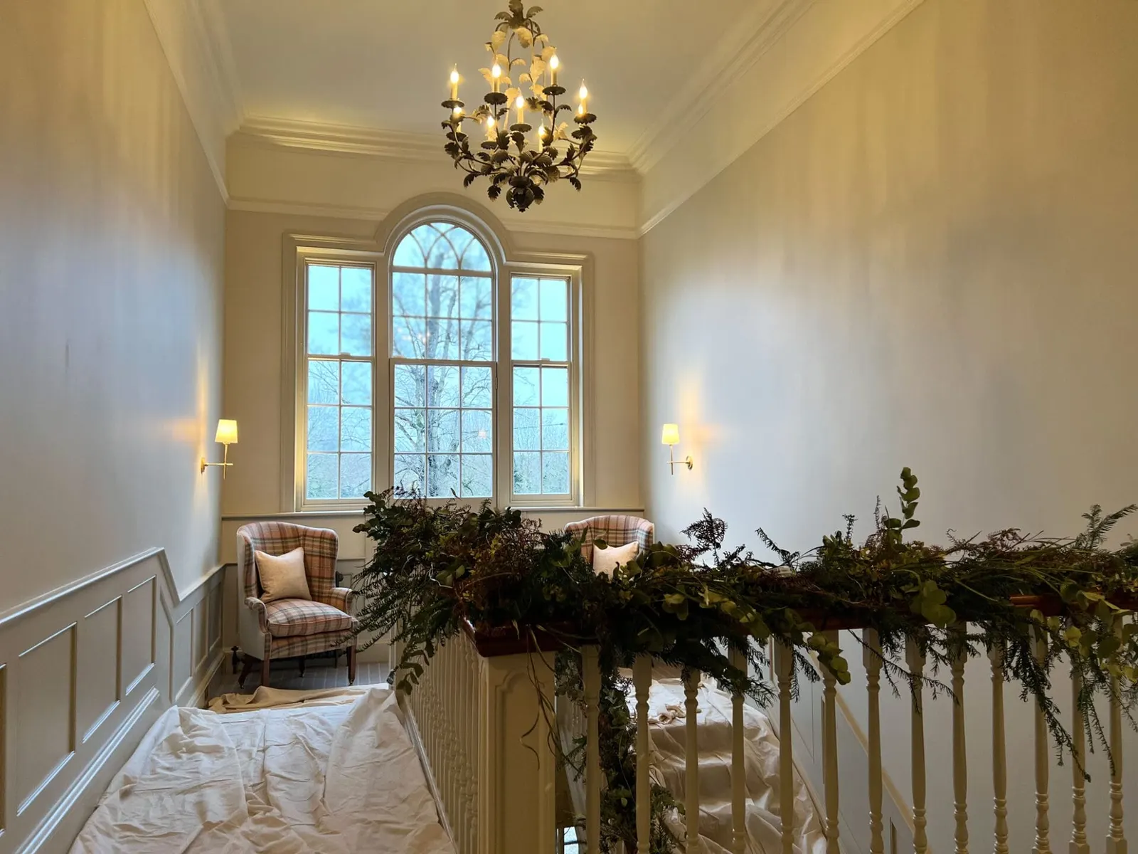 The stair hall with an arched window and wall lights, a garland dressed along the banister.
