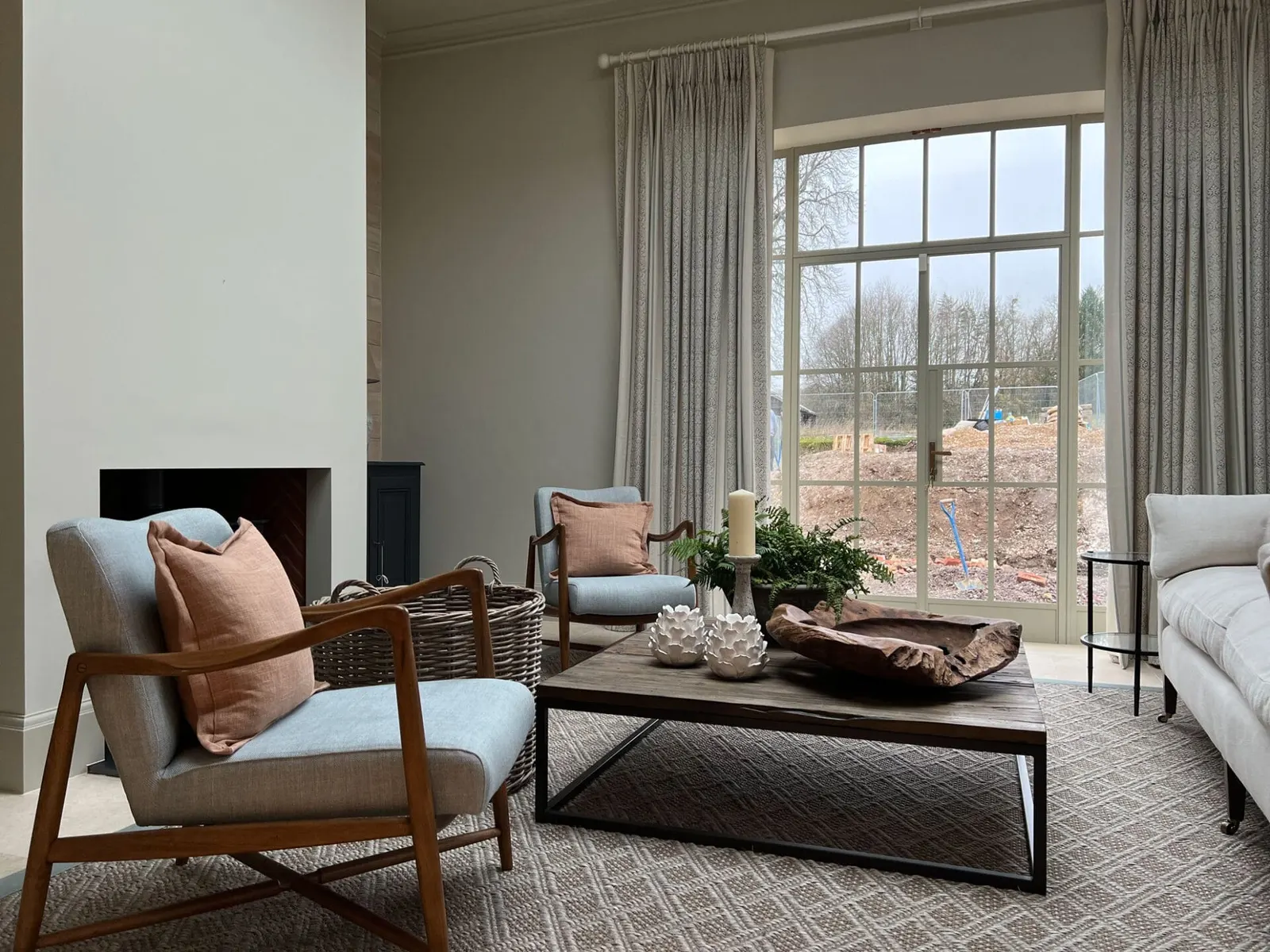A pale reception room with a large window, low table and a plain chimneypiece.
