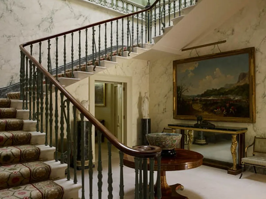 The stair hall, its walls worked in a marbled finish, with an iron balustrade and an oil painting on the half-landing.