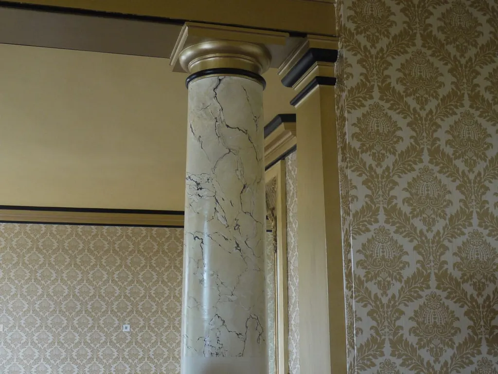 A marbled pilaster meeting damask wall covering, the joint worked by hand.