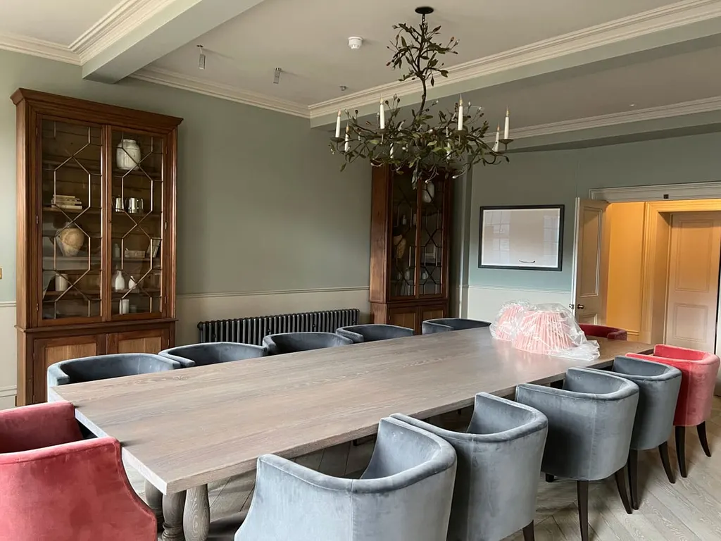 The dining room, long table set with velvet chairs beneath a chandelier, glazed cabinet behind.