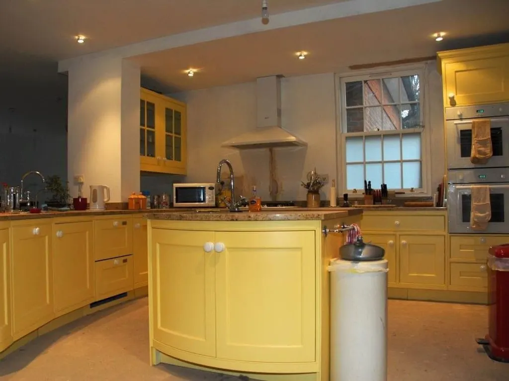 A yellow painted kitchen with a curved island, timber worktops and a range in the chimney breast.