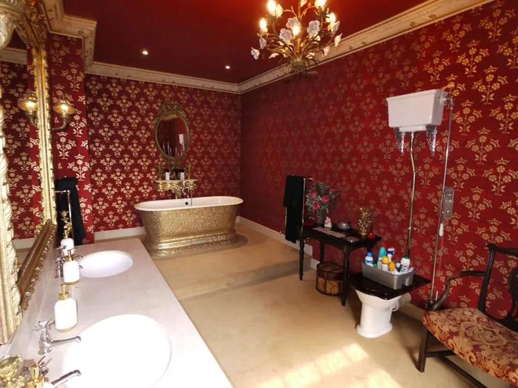 A bathroom papered in red damask, with a copper roll-top bath and a chandelier.